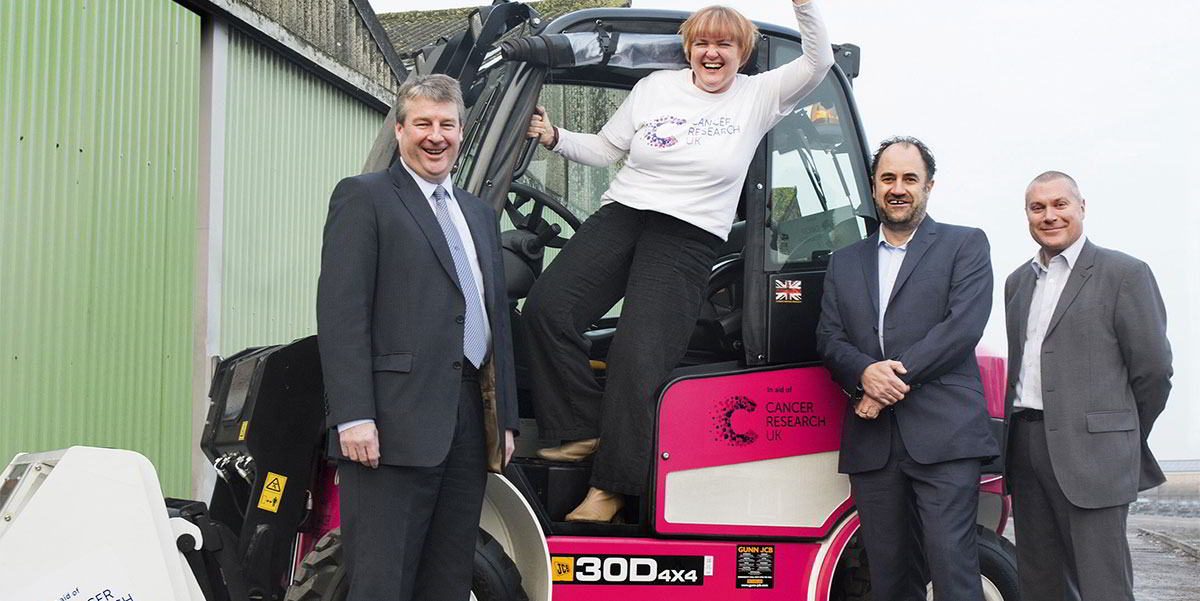 Group beside a pink-and-white Cancer Research UK JCB mini excavator