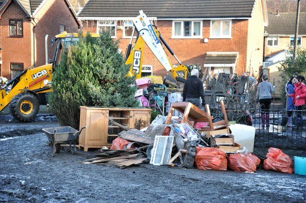 JCB backhoe loader helping clear flood-damaged furniture and debris from a residential street