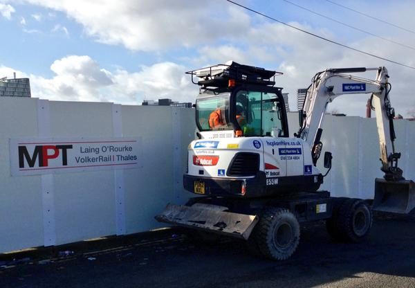 White wheeled excavator beside tram construction hoardings