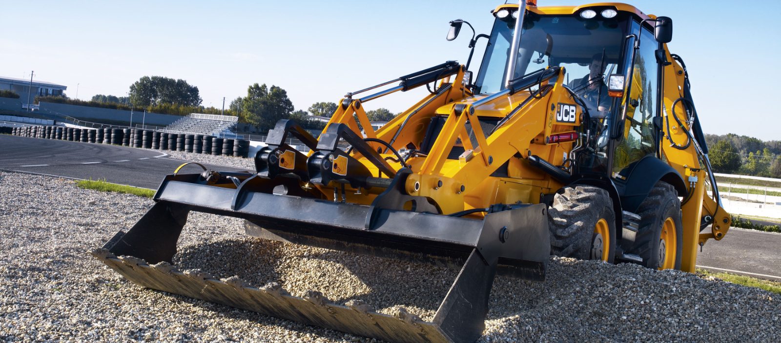 JCB backhoe loader with a wide front bucket on a gravel site