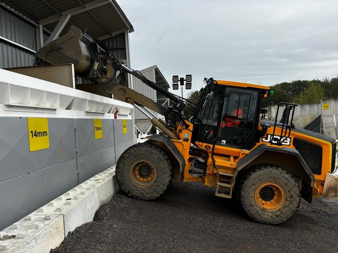 JCB loading shovel with its bucket raised over an aggregate bay