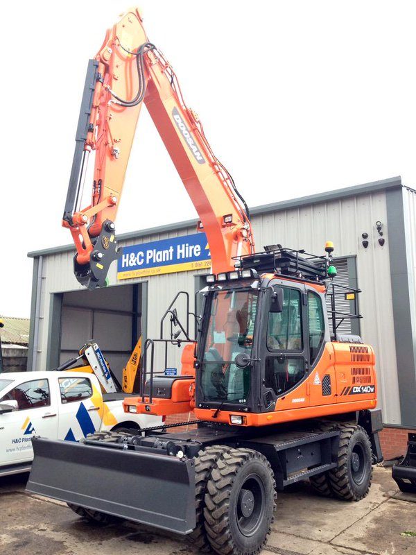 Orange wheeled excavator with a front blade outside the H&C workshop