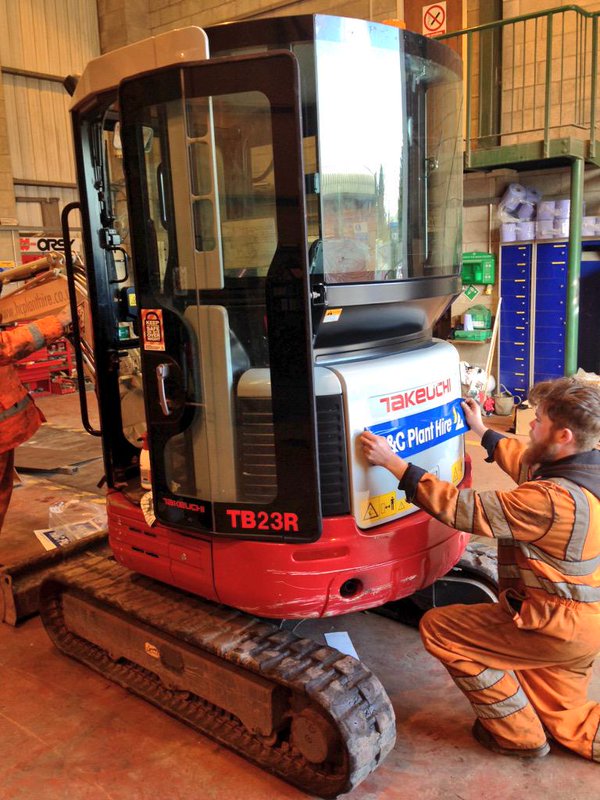 Worker applying H&C signage to the side of a Takeuchi mini excavator