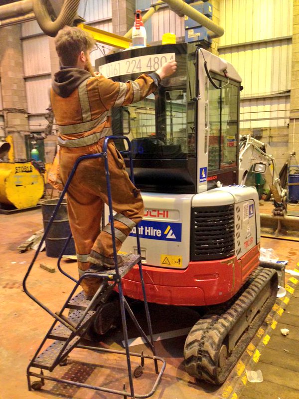 Worker fitting signage to a Takeuchi mini excavator inside the workshop
