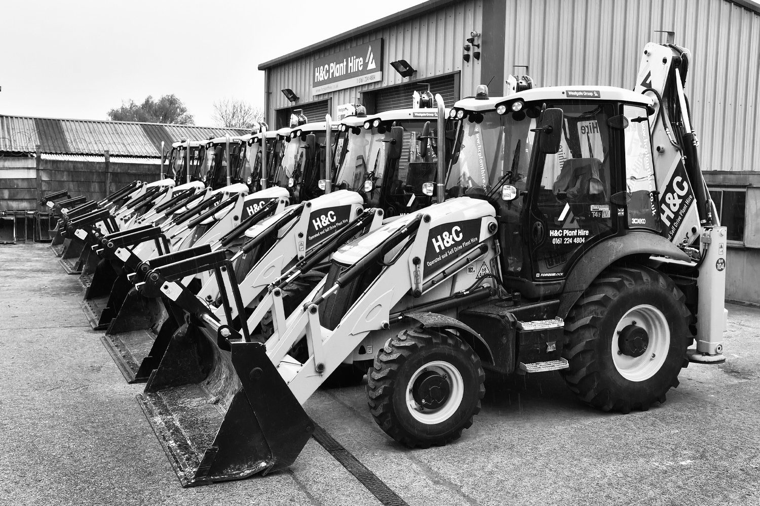 Black-and-white photograph of H&C backhoe loaders lined up outside the workshop