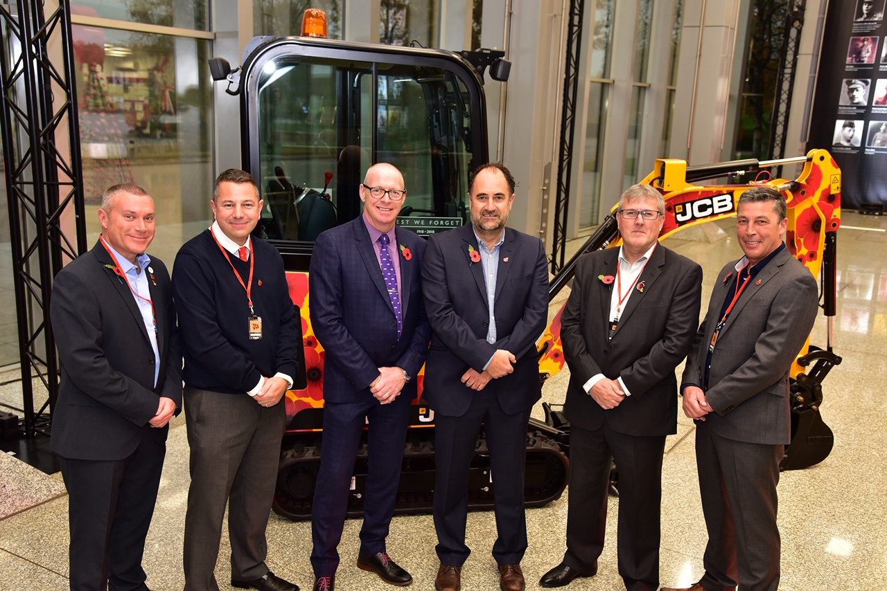 Group photograph in front of a poppy-liveried JCB mini excavator