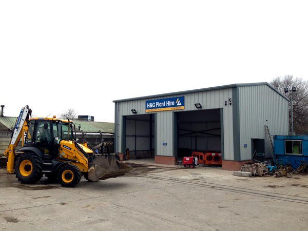 H&C workshop with two vehicle bays and a backhoe loader outside